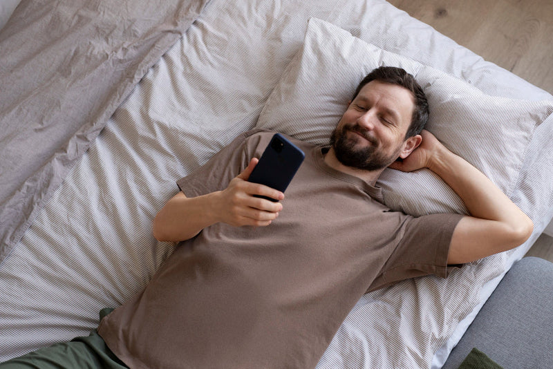 Man in bed glimlacht naar telefoon