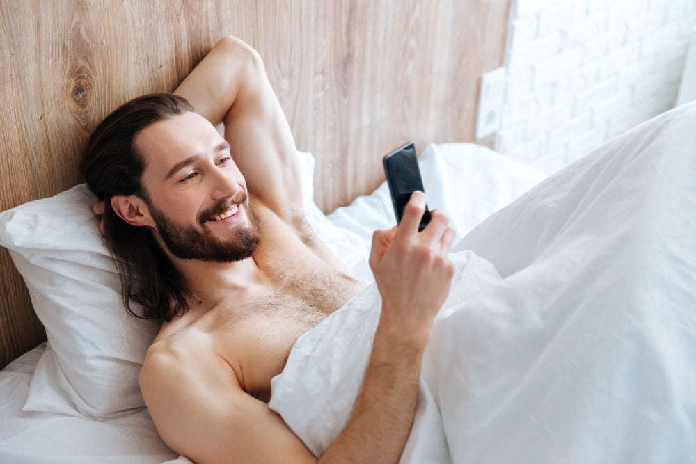 Man glimlacht naar telefoon en ligt in bed